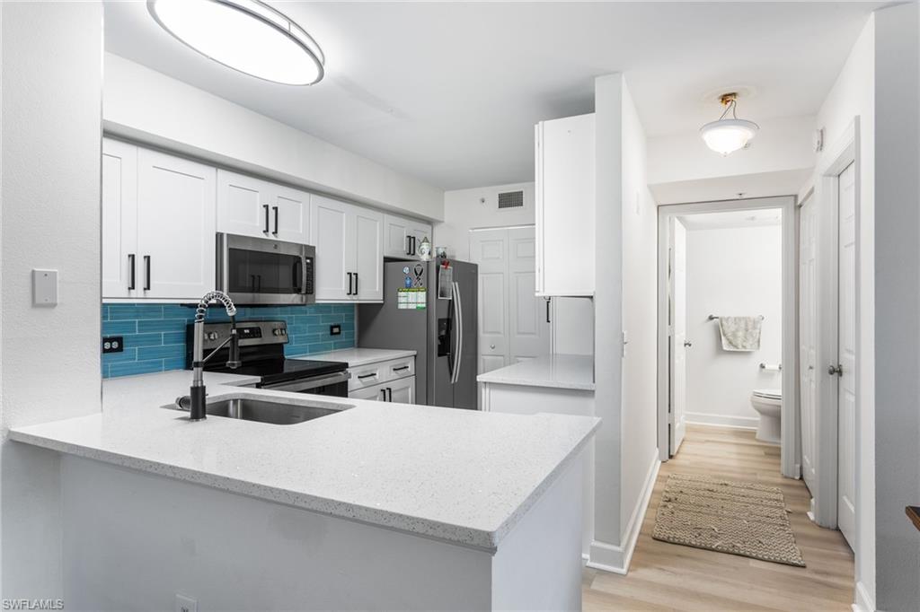 Kitchen with white cabinets, stainless steel appliances, tasteful backsplash, a peninsula, and light wood-style floors