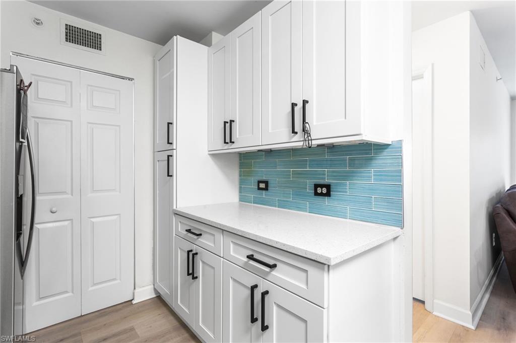 Kitchen featuring stainless steel fridge, light wood-style floors, light stone countertops, and white cabinets