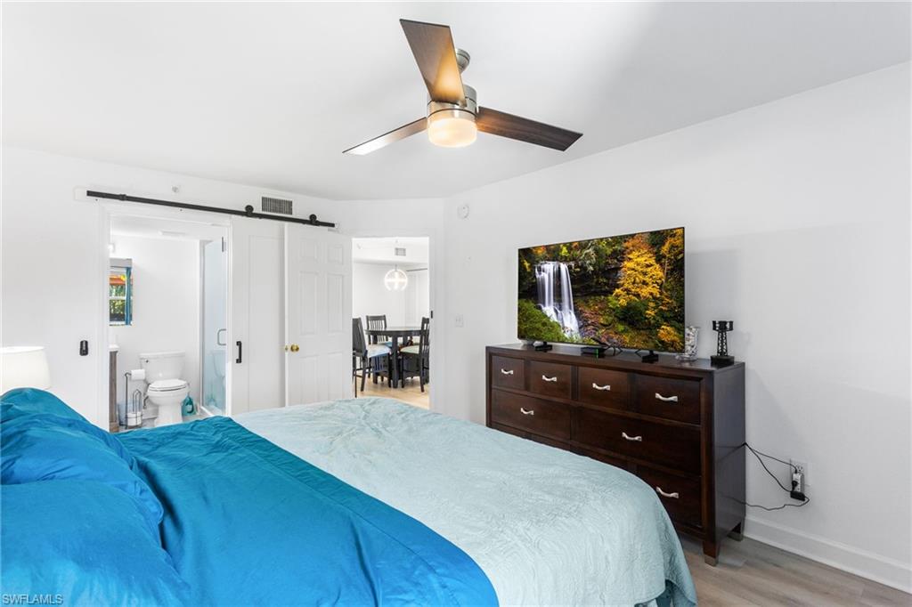 Bedroom featuring a barn door, ceiling fan, ensuite bathroom, and light wood-style flooring