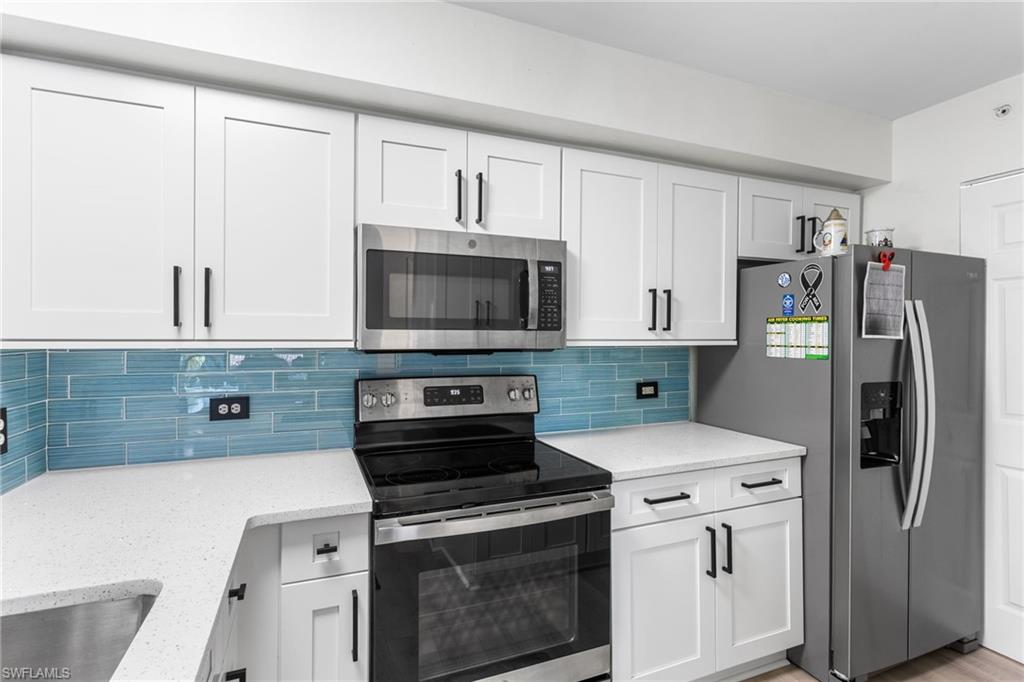 Kitchen featuring stainless steel appliances, white cabinets, decorative backsplash, and light stone counters