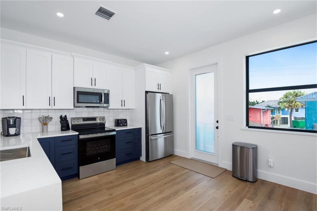 Kitchen with white cabinetry, stainless steel appliances, backsplash, light stone counters, and recessed lighting