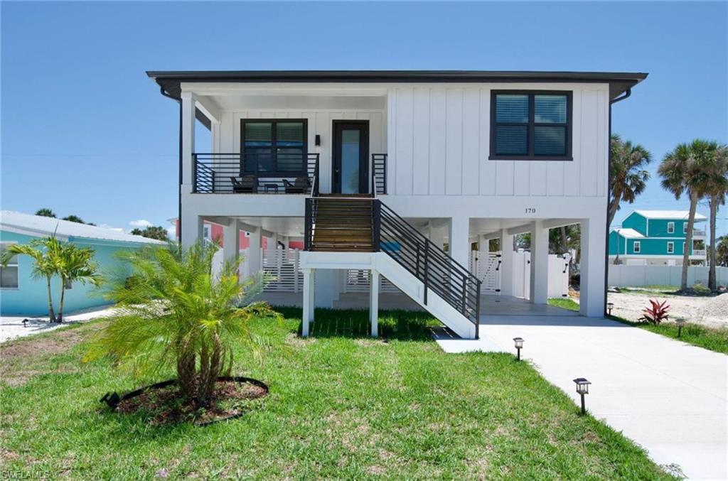 View of front of home with a carport, stairway, concrete driveway, a front lawn, and board and batten siding - Virtually Edited Image