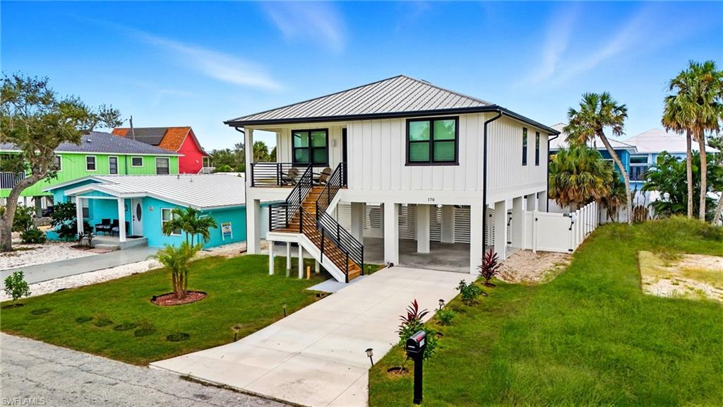 View of front of house featuring a carport, stairway, concrete driveway, board and batten siding, and a metal roof - Virtually Edited Image