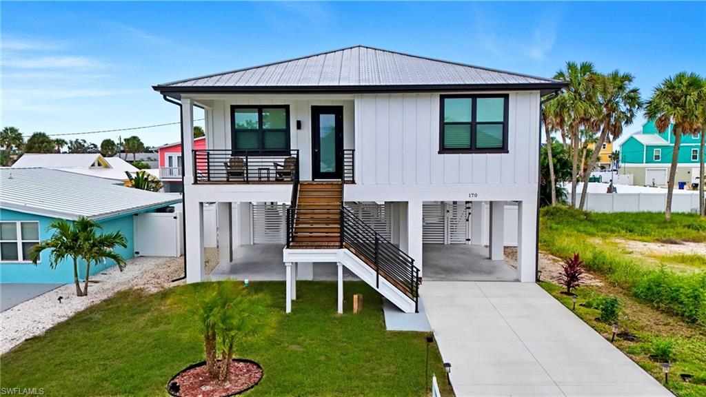 Rear view of property featuring a carport, stairway, a metal roof, concrete driveway, and board and batten siding - Virtually Edited Image