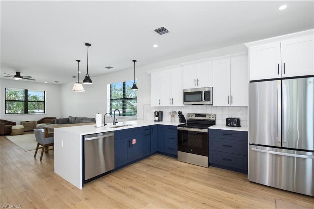 Kitchen featuring white cabinetry, stainless steel appliances, open floor plan, pendant lighting, and decorative backsplash - Virtually Edited Image