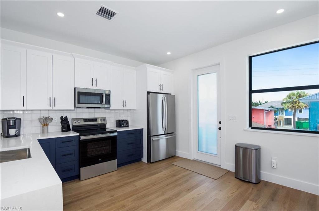 Kitchen featuring white cabinetry, stainless steel appliances, light stone countertops, decorative backsplash, and recessed lighting - Virtually Edited Image
