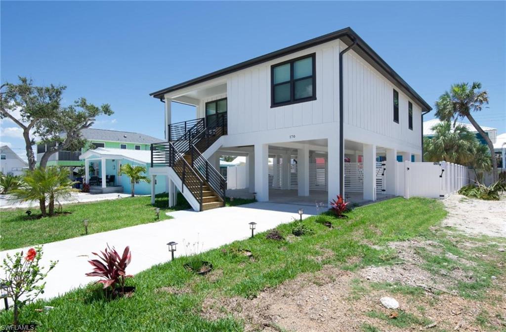 View of front facade with a carport, a patio, concrete driveway, stairs, and a gate - Virtually Edited Image