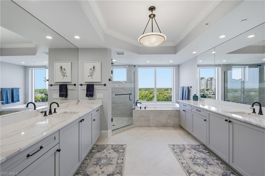 Bathroom featuring crown molding, a bath, two vanities, a stall shower, and recessed lighting