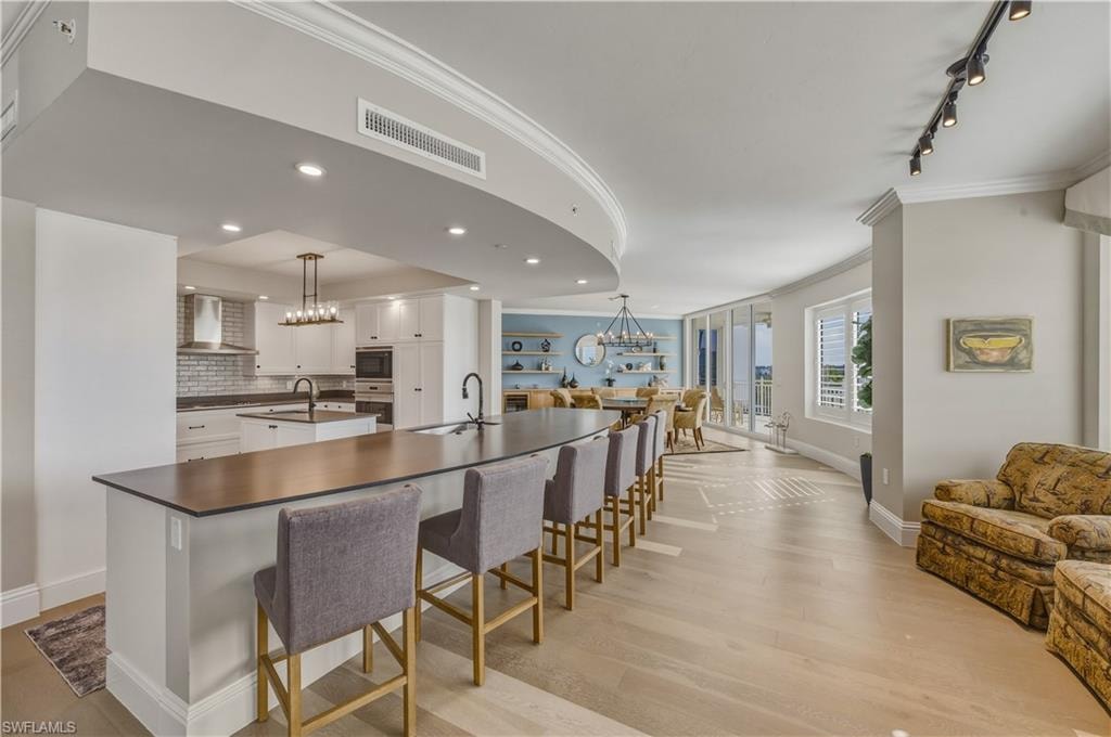 Kitchen with ornamental molding, open floor plan, white cabinets, tasteful backsplash, and a kitchen bar