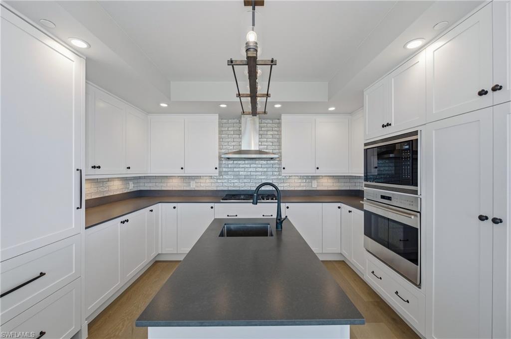 Kitchen featuring dark countertops, white cabinets, stainless steel appliances, decorative light fixtures, and a raised ceiling