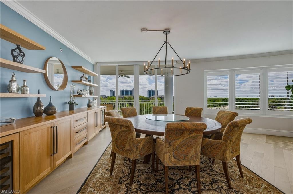 Dining area with a chandelier, crown molding, light wood-style floors, a ceiling fan, and wine cooler