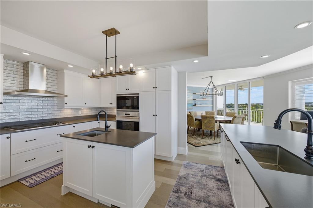 Kitchen with dark countertops, backsplash, suspended lighting, light wood-style floors, and white cabinets
