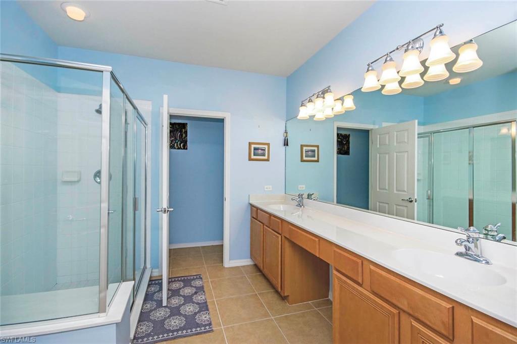 Bathroom with double vanity, a shower stall, and light tile patterned flooring