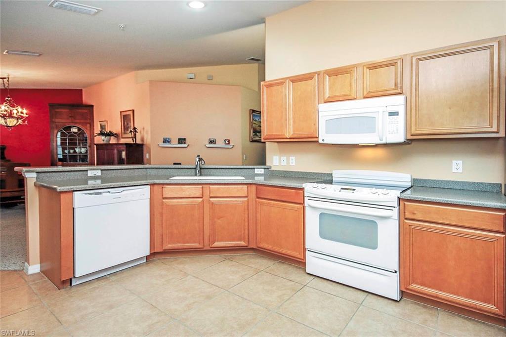 Kitchen with white appliances, a peninsula, hanging lights, and light tile patterned floors