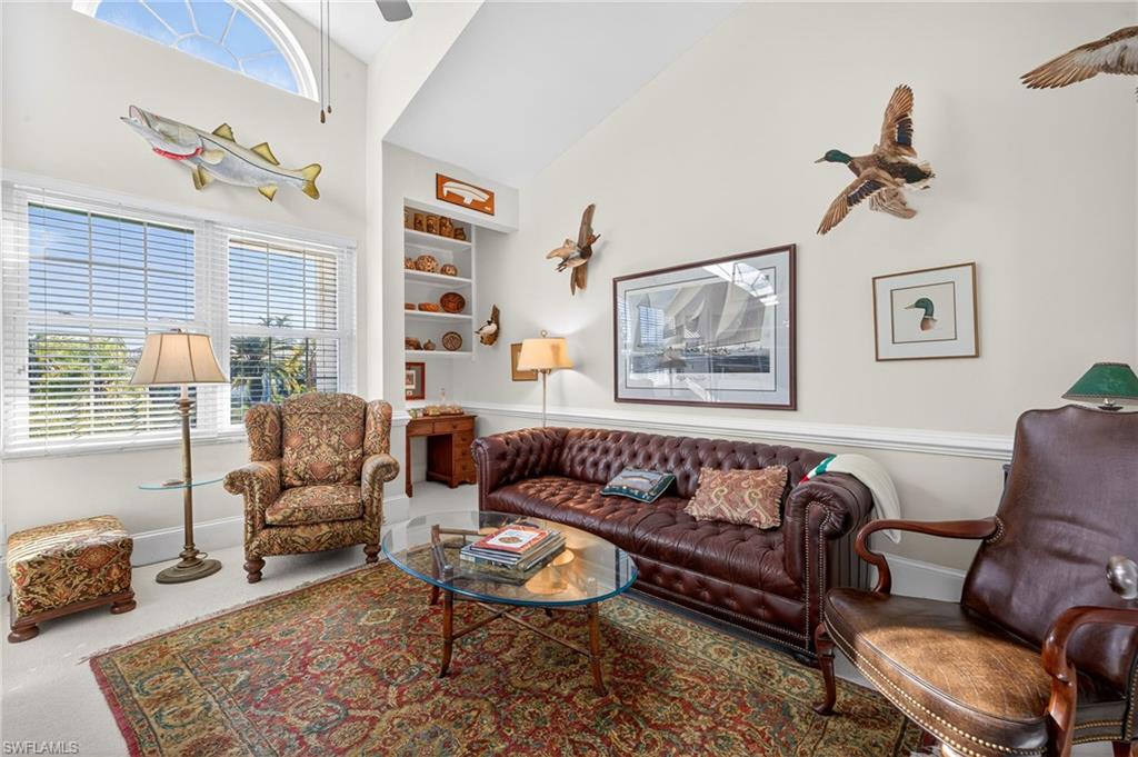 Living area with built in shelves, healthy amount of natural light, a ceiling fan, and lofted ceiling