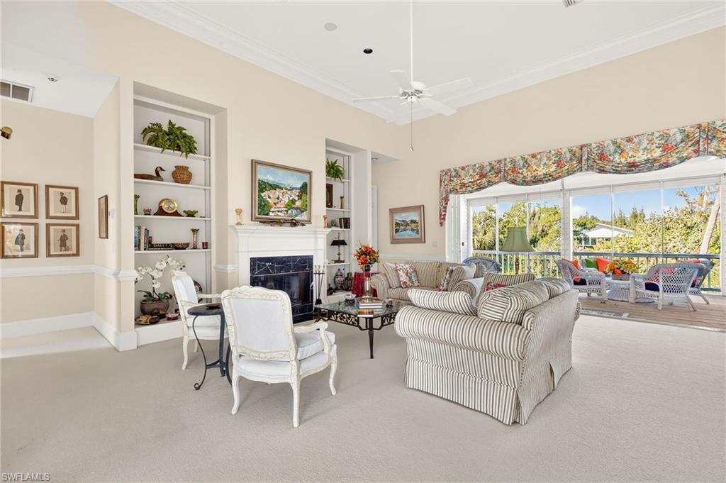 Carpeted living room with built in features, crown molding, a fireplace, and a ceiling fan