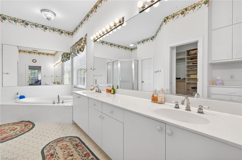 Full bathroom featuring a bath, double vanity, a shower stall, a walk in closet, and light tile patterned floors