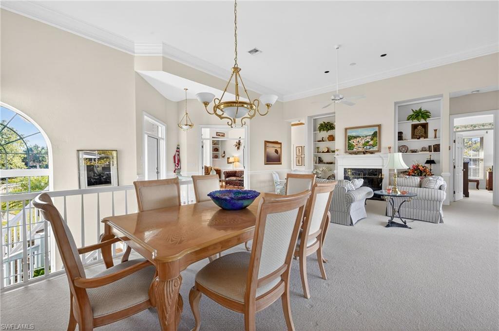 Carpeted dining area featuring ornamental molding, suspended lighting, a fireplace, built in features, and ceiling fan