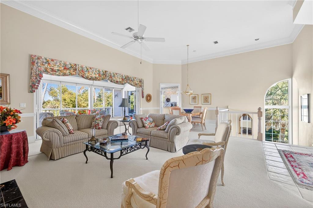 Carpeted living room featuring a ceiling fan, crown molding, plenty of natural light, and a high ceiling