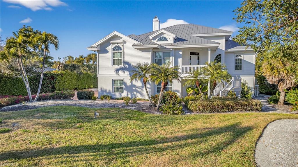Coastal inspired home featuring a front lawn, a chimney, a metal roof, and covered porch