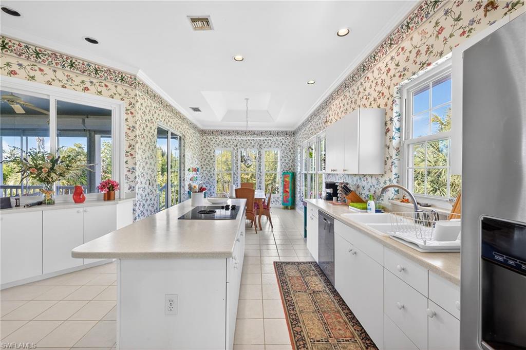 Kitchen with stainless steel appliances, wallpapered walls, crown molding, white cabinets, and light countertops