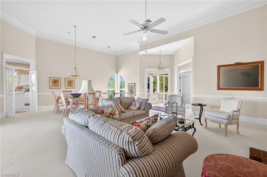 Living area featuring crown molding, suspended lighting, carpet flooring, a ceiling fan, and a high ceiling