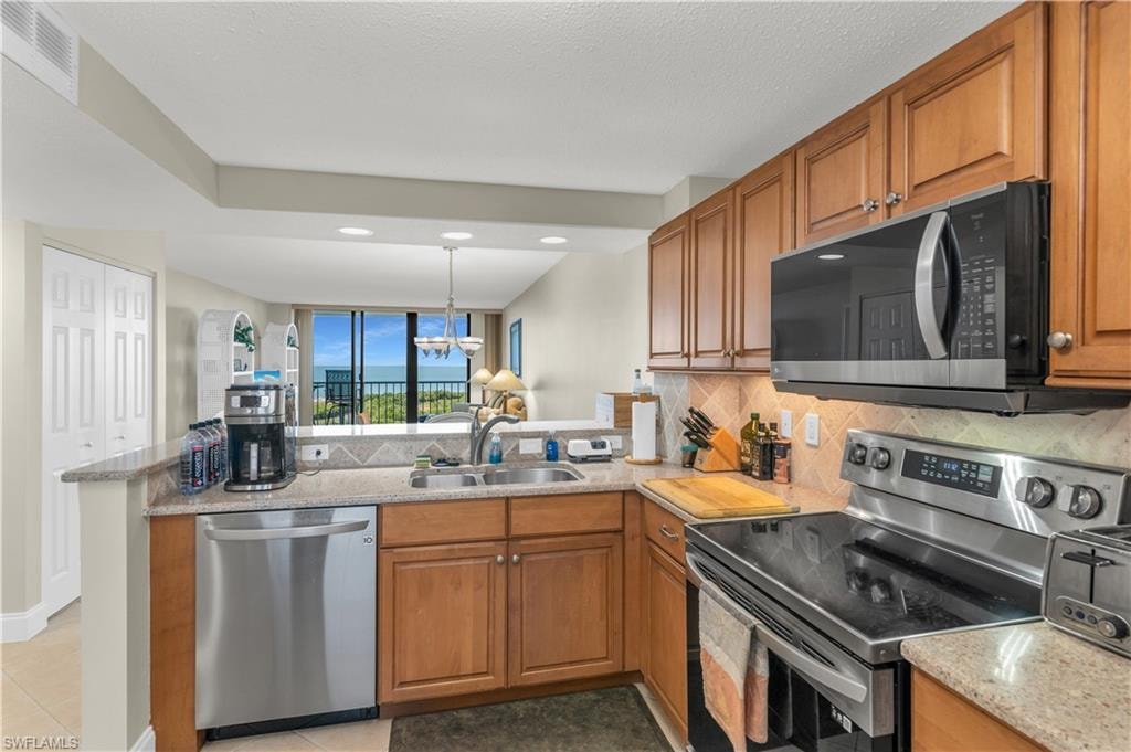 Kitchen featuring stainless steel appliances, wood finish cabinetry, a peninsula, and light stone countertops