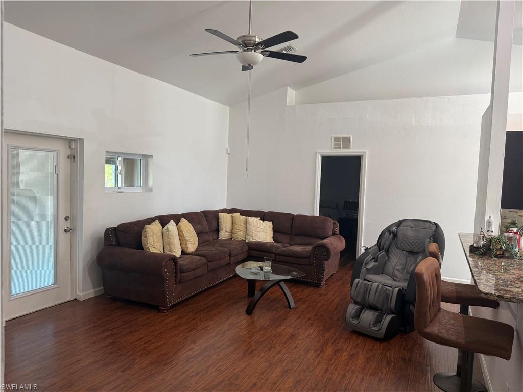 Living room view from the kitchen featuring dark wood-style floors, ceiling fan, and lofted ceiling with storage compartment
