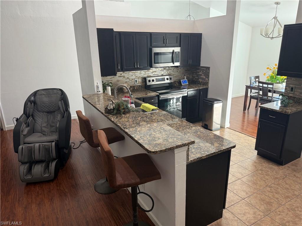 Kitchen with dark cabinetry, dark stone countertops, a peninsula, stainless steel appliances, and a kitchen bar