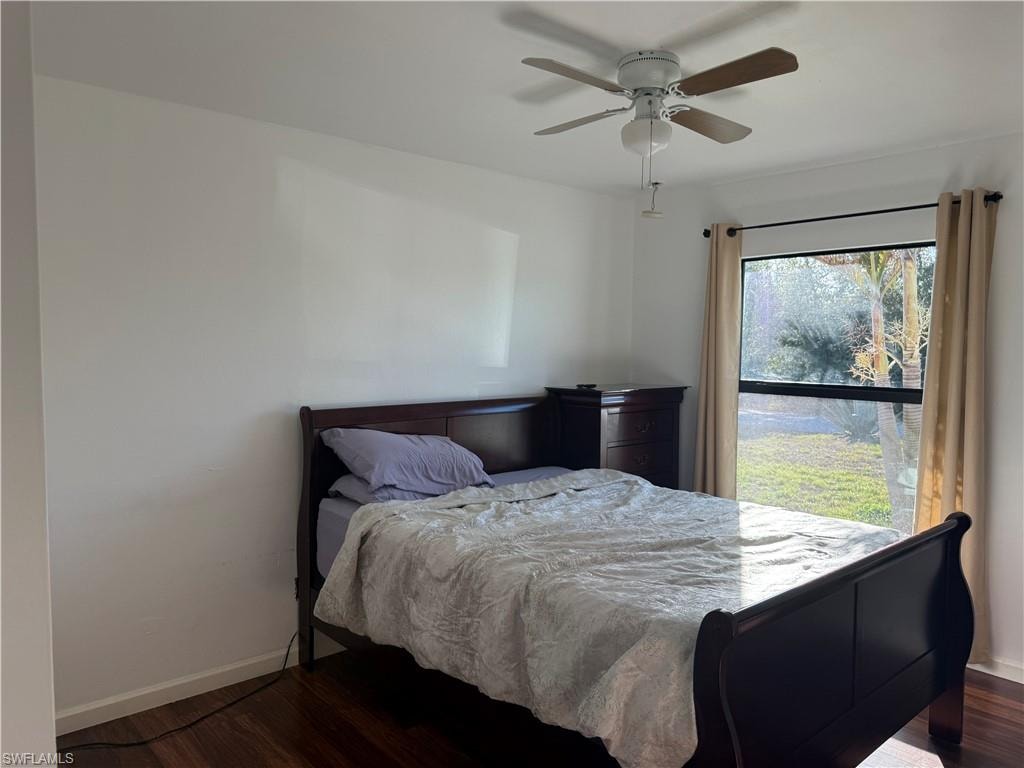 1st guest bedroom one featuring dark wood-style flooring and a ceiling fan with view of the front yard