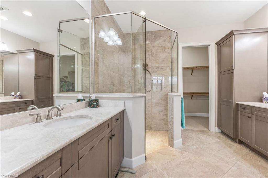 Full bathroom featuring two vanities, a walk in closet, and walk in shower