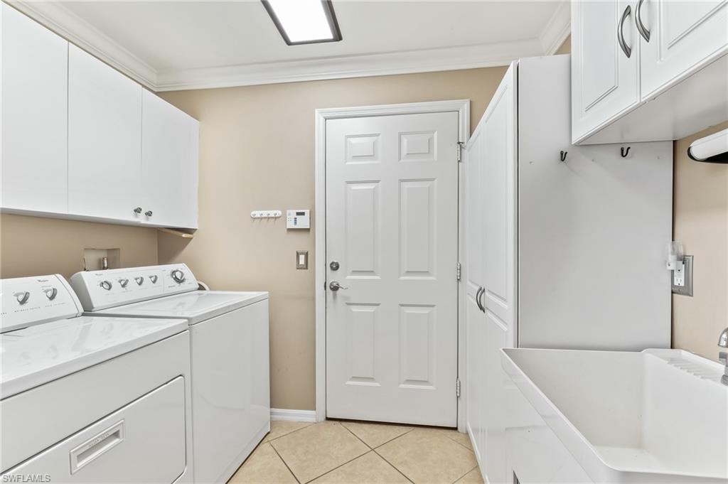 Laundry room featuring washing machine and dryer, light tile patterned flooring, crown molding, and cabinet space
