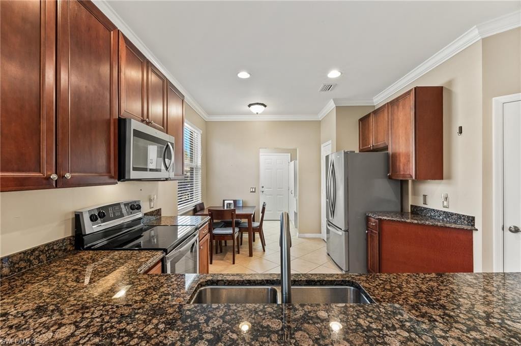 Kitchen featuring stainless steel appliances, ornamental molding, dark stone countertops, light tile patterned flooring, and recessed lighting