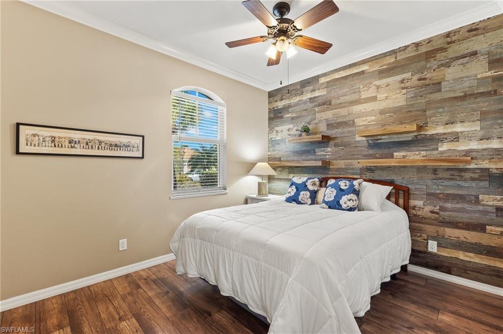 Bedroom with wood walls, ornamental molding, wood finished floors, an accent wall, and a ceiling fan
