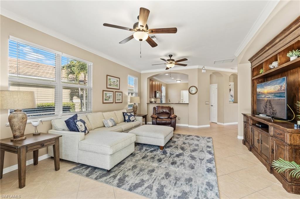 Living area featuring arched walkways, ornamental molding, ceiling fan, and light tile patterned flooring