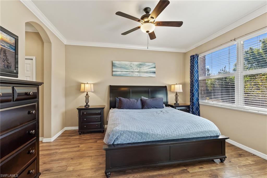 Bedroom with hardwood / wood-style floors, ornamental molding, ceiling fan, and arched walkways