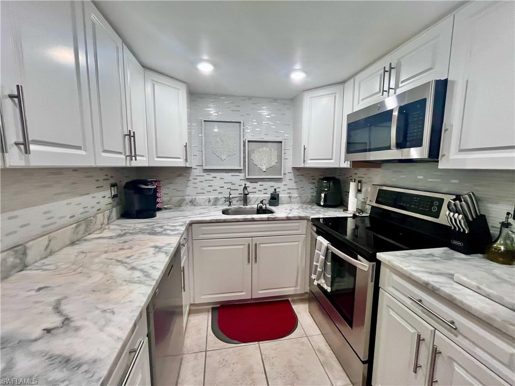 Kitchen featuring appliances with stainless steel finishes, white cabinetry, tasteful backsplash, light tile patterned floors, and light granite counters