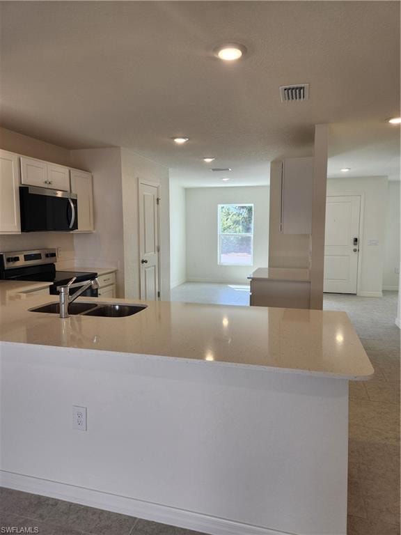 Kitchen with light stone countertops, a peninsula, range, white cabinets, and recessed lighting
