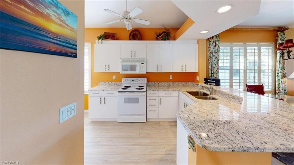 Kitchen with white appliances, a peninsula, light stone counters, white cabinets, and recessed lighting