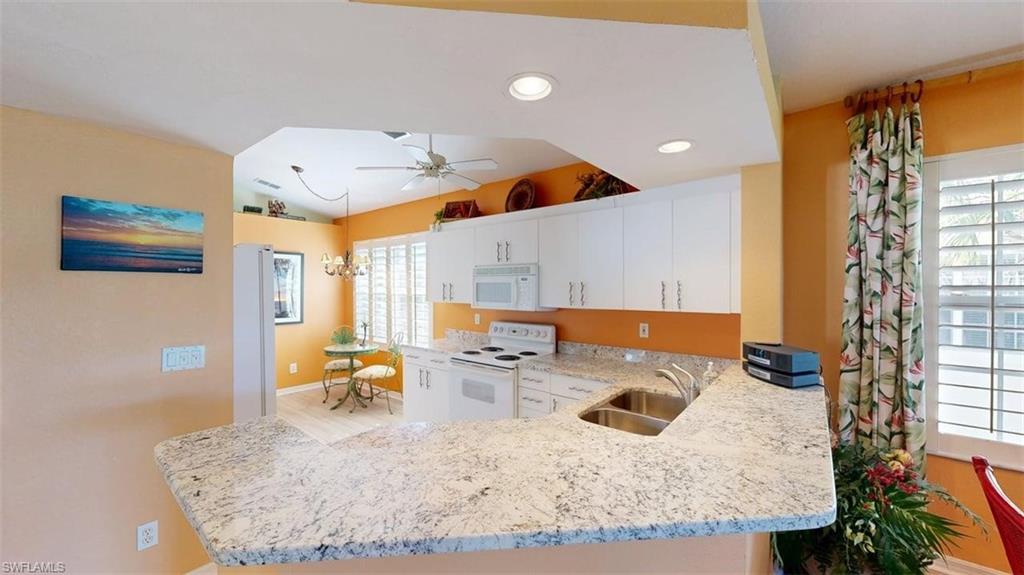 Kitchen featuring a peninsula, white appliances, ceiling fan, light stone countertops, and white cabinetry
