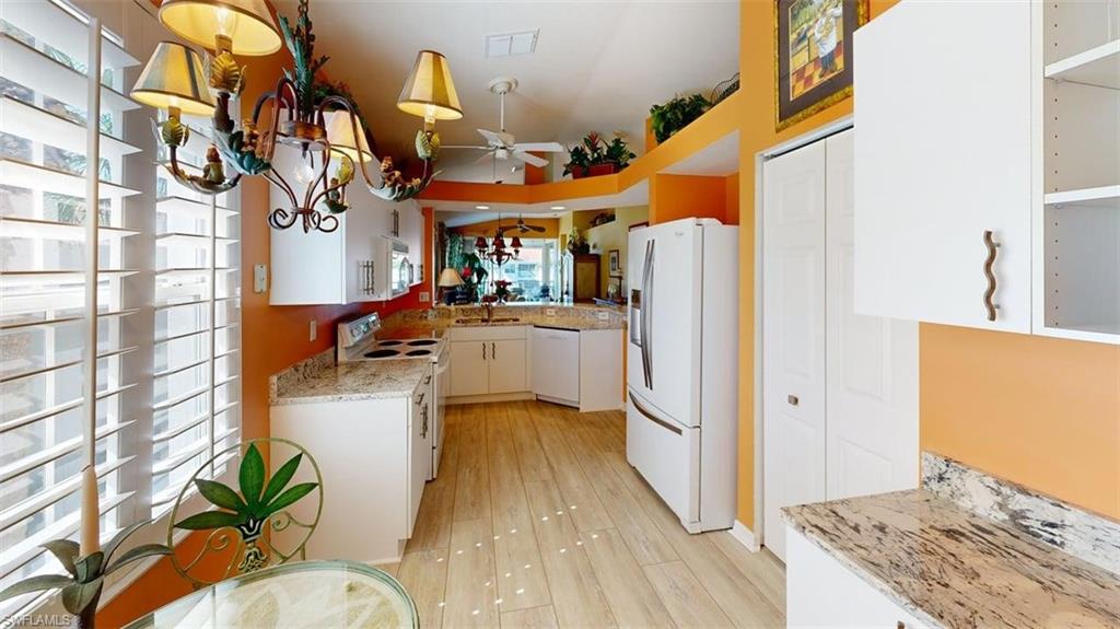 Kitchen featuring white appliances, light stone counters, ceiling fan, white cabinets, and hanging light fixtures