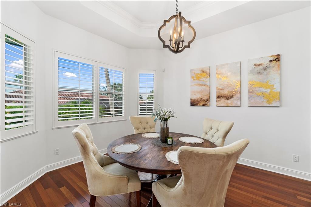 Dining room featuring a tray ceiling, dark wood finished floors, a chandelier, and ornamental molding