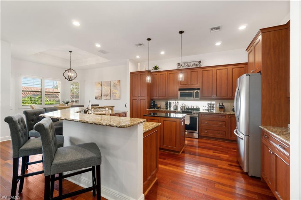 Kitchen featuring wood finish cabinetry, dark stone counters, stainless steel appliances, dark wood-type flooring, and a tray ceiling