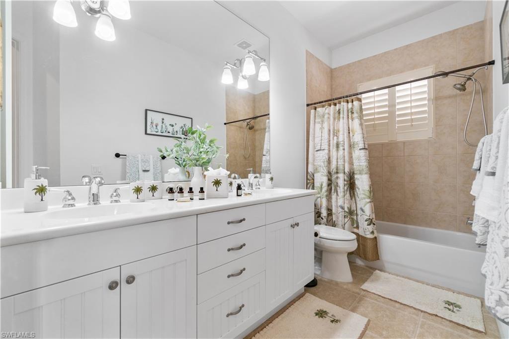 Bathroom featuring double vanity, shower / bath combination with curtain, light tile patterned floors, and suspended lighting