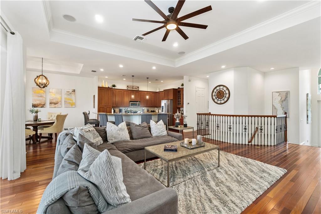 Living area featuring ceiling fan, light wood-type flooring, a raised ceiling, crown molding, and suspended lighting
