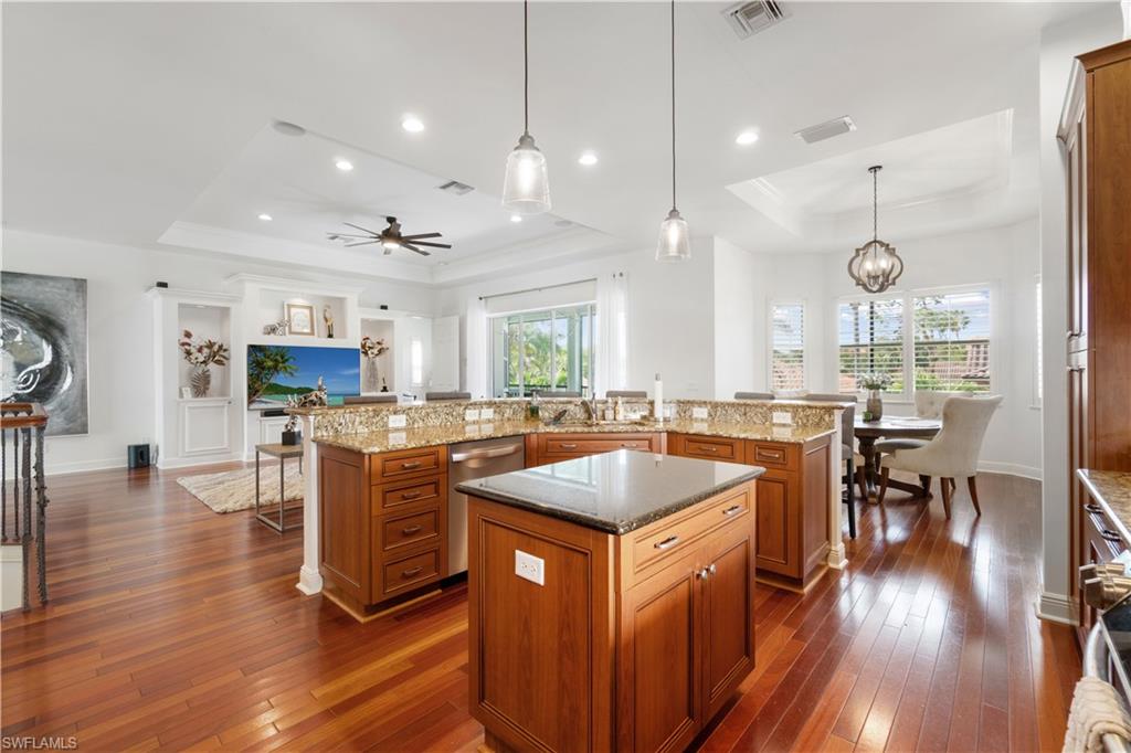 Kitchen with dark stone counters, a tray ceiling, dark wood-style floors, open floor plan, and ornamental molding