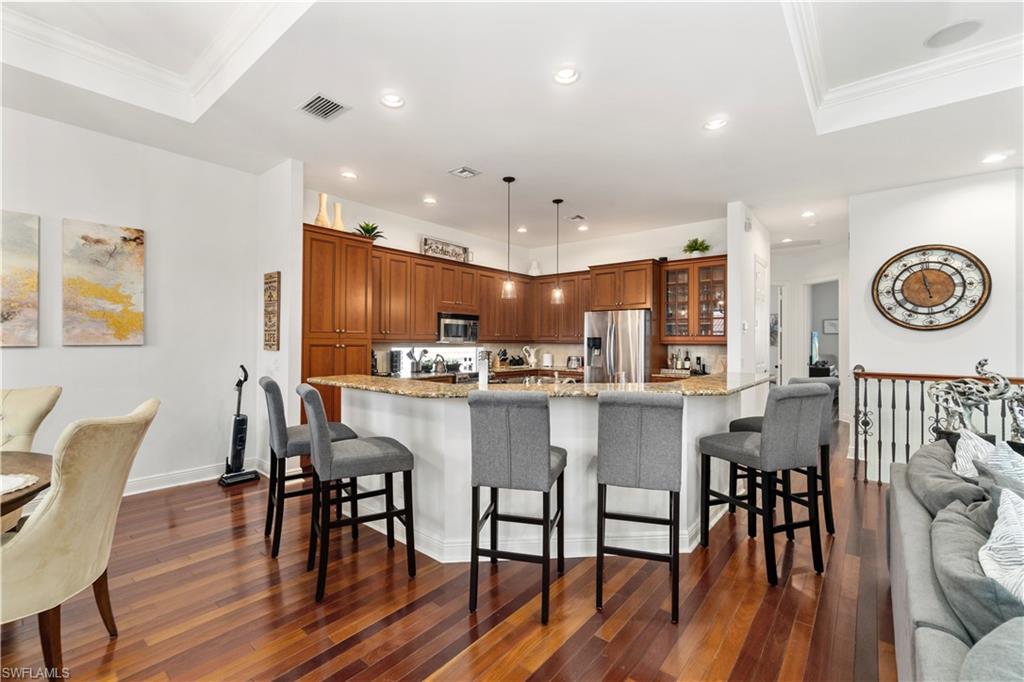 Kitchen featuring a breakfast bar, wood finish cabinetry, pendant lighting, light stone countertops, and dark wood-style flooring