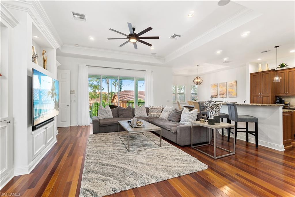 Living room featuring dark wood-type flooring, ceiling fan, ornamental molding, and a raised ceiling
