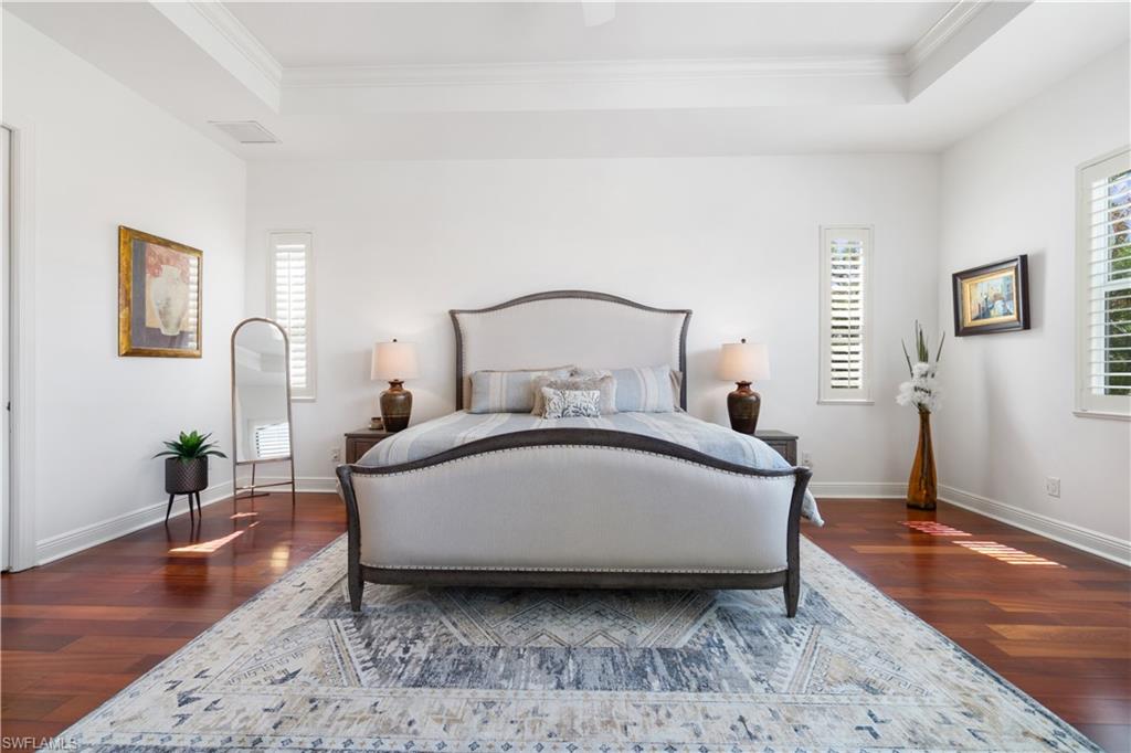 Bedroom with a tray ceiling, ornamental molding, dark wood-style floors, and a ceiling fan