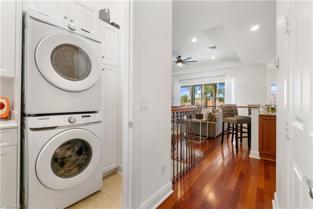 Laundry area with stacked washer / drying machine, a tray ceiling, cabinet space, dark wood-type flooring, and recessed lighting